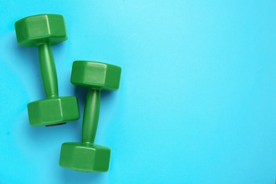 Photo of Green dumbbells on light blue background, flat lay. Space for text