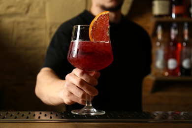 Bartender holding glass of fresh alcoholic cocktail in bar, closeup