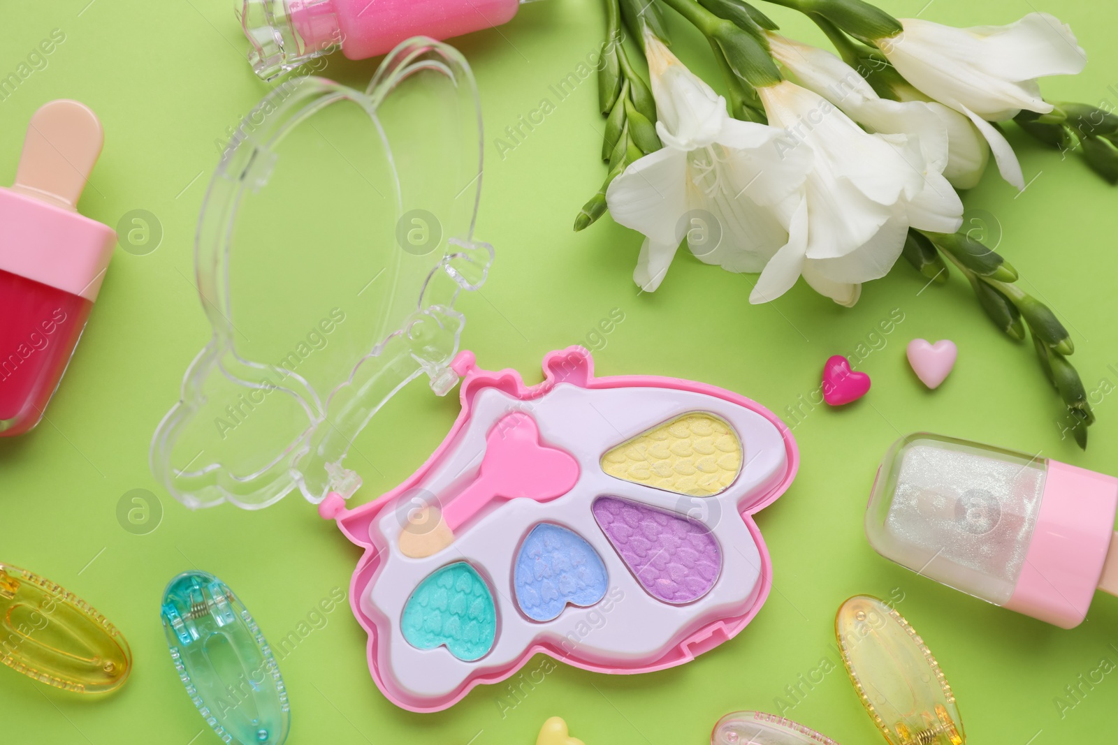 Photo of Decorative cosmetics for kids. Eye shadow palette, accessories and flowers on light green background, flat lay