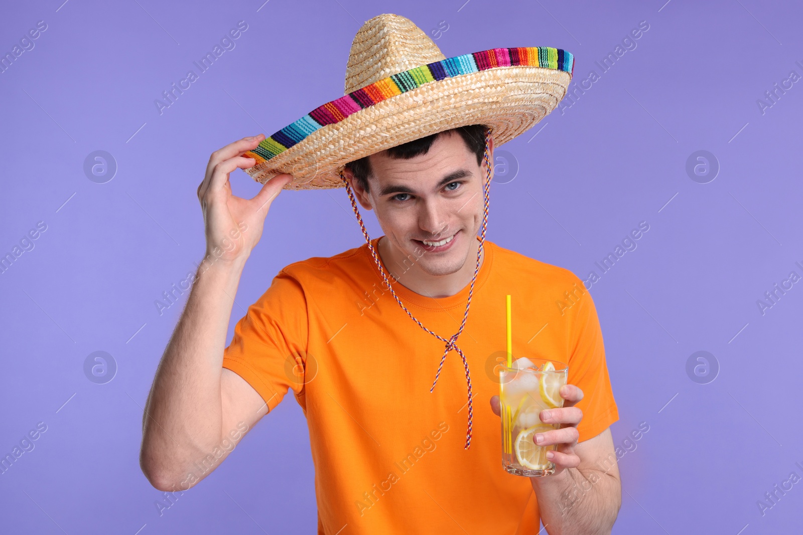 Photo of Young man in Mexican sombrero hat with cocktail on violet background