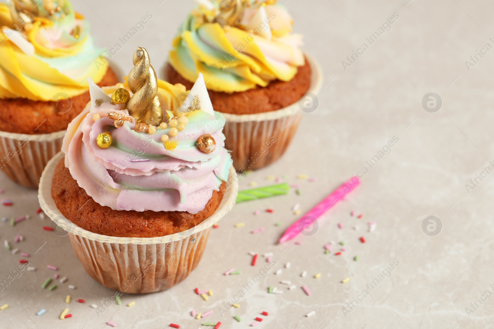 Photo of Cute sweet unicorn cupcakes on beige marble table, closeup. Space for text