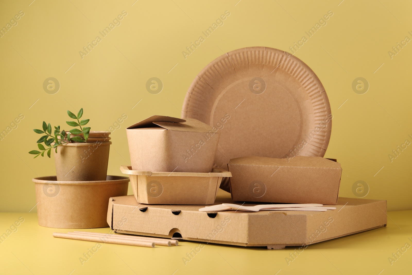 Photo of Eco friendly food packaging. Paper containers, tableware and green twigs on pale yellow background