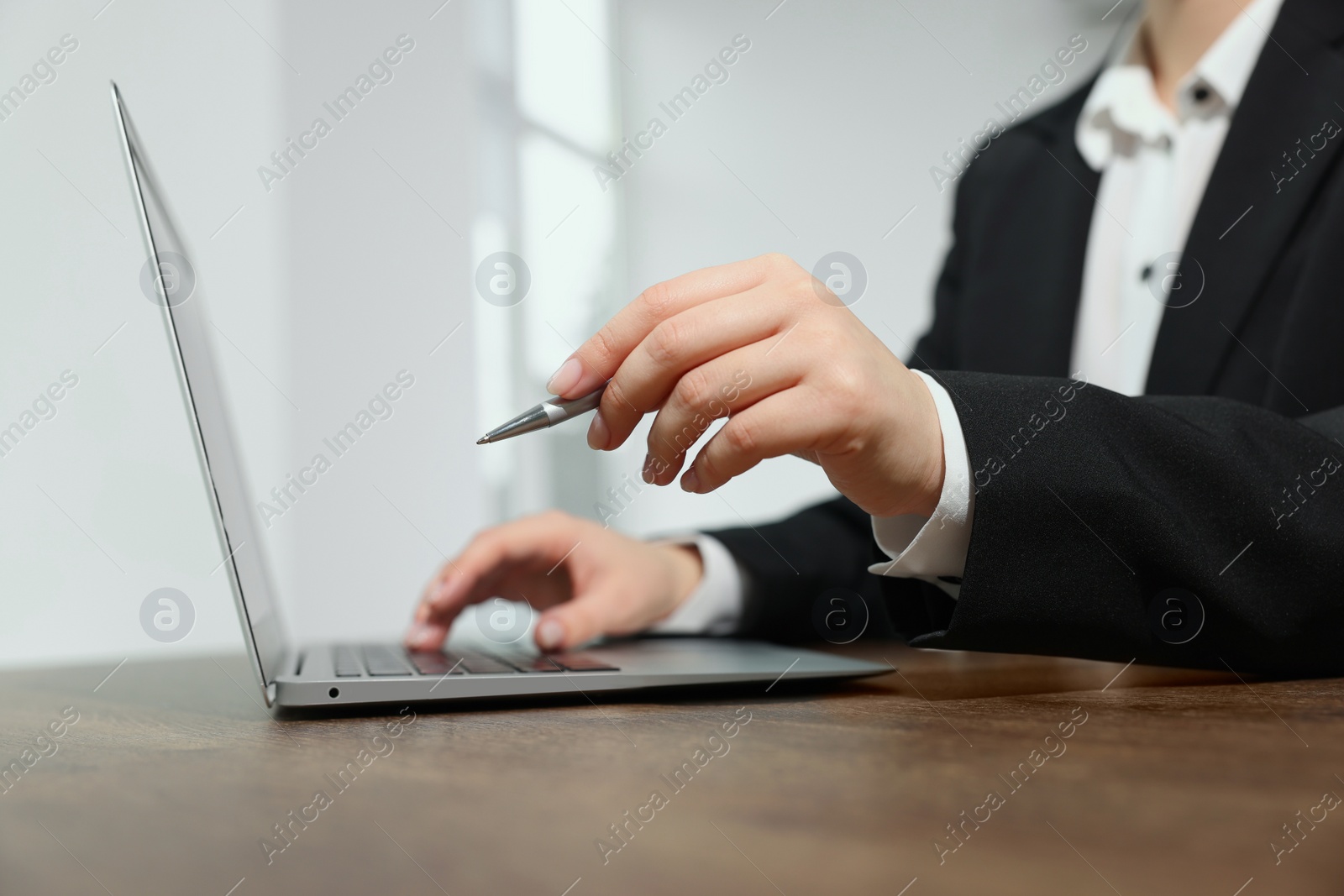 Photo of Woman with pen working on laptop at wooden table, closeup. Electronic document management