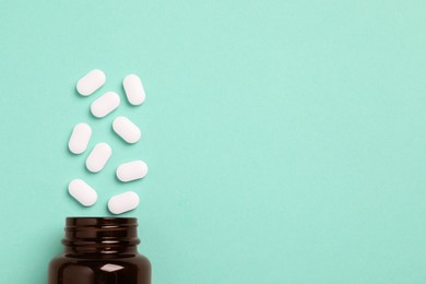 Photo of Plastic medical bottle with many pills on turquoise background, flat lay. Space for text