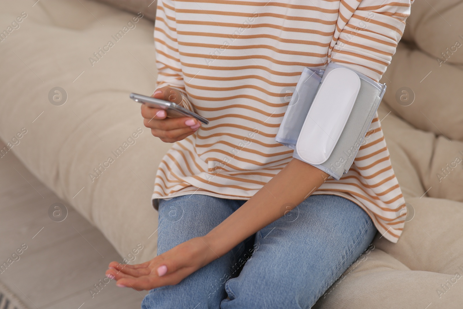 Photo of Woman checking blood pressure with modern monitor and smartphone indoors, closeup