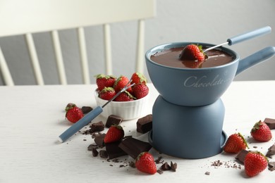Photo of Fondue pot with chocolate and fresh strawberries on white table