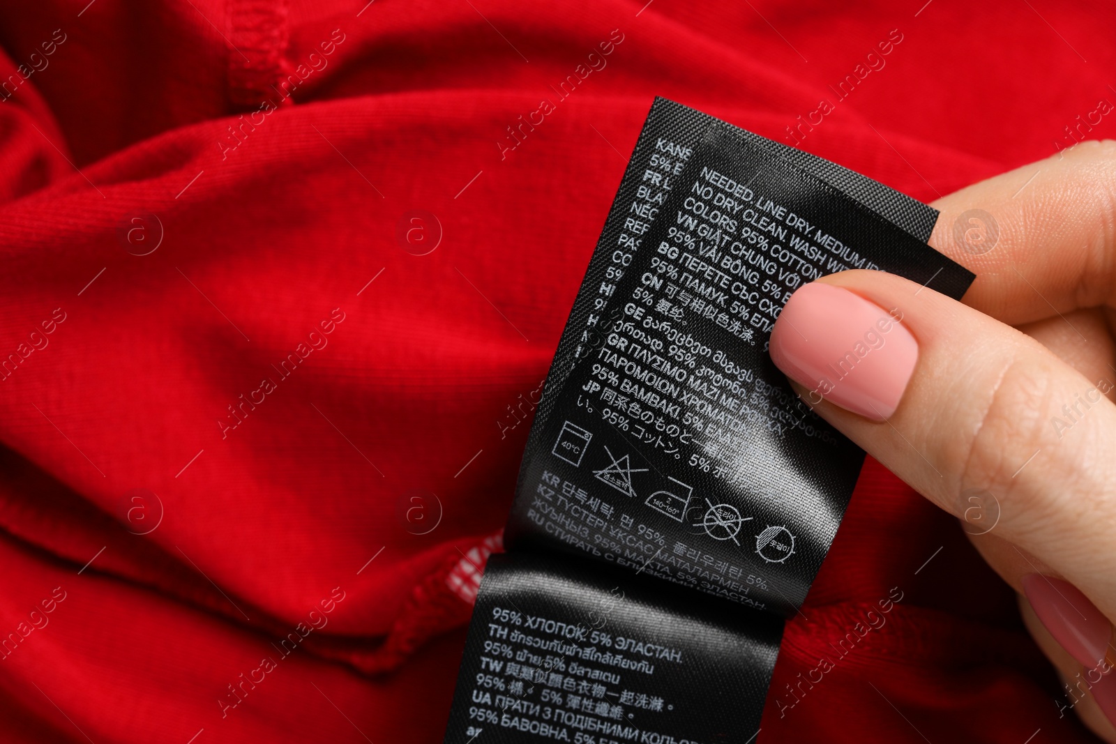 Photo of Woman holding clothing labels on red garment, closeup. Space for text