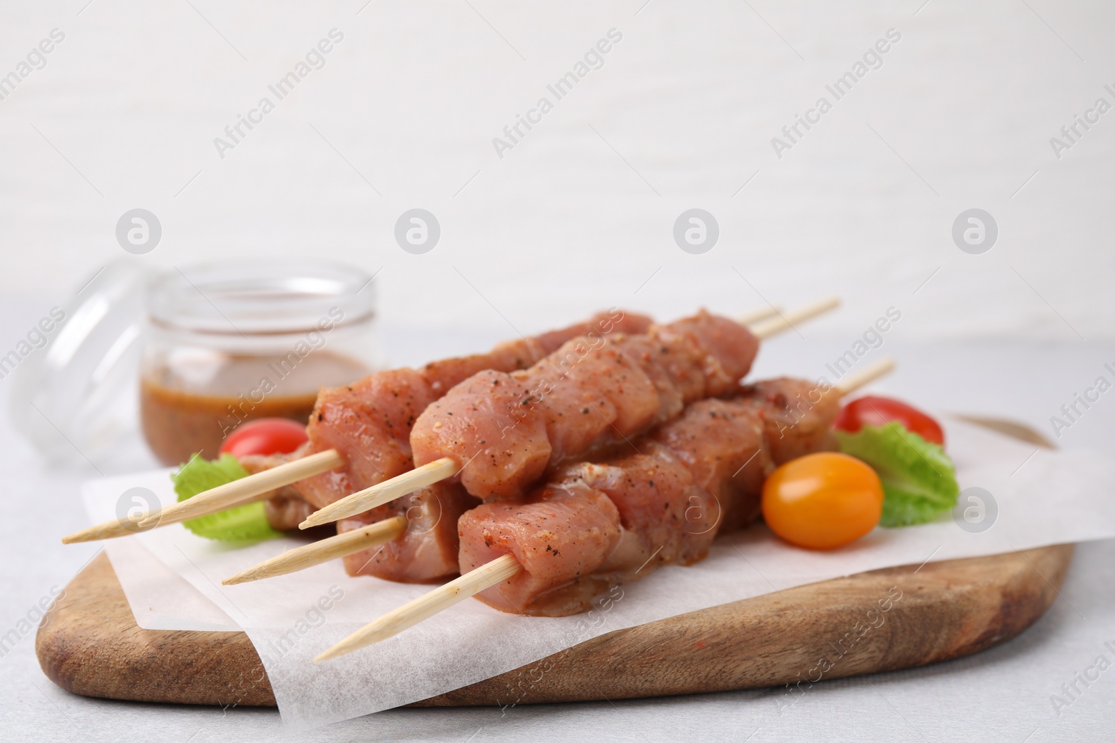 Photo of Wooden skewers with cut raw marinated meat on light grey table, closeup