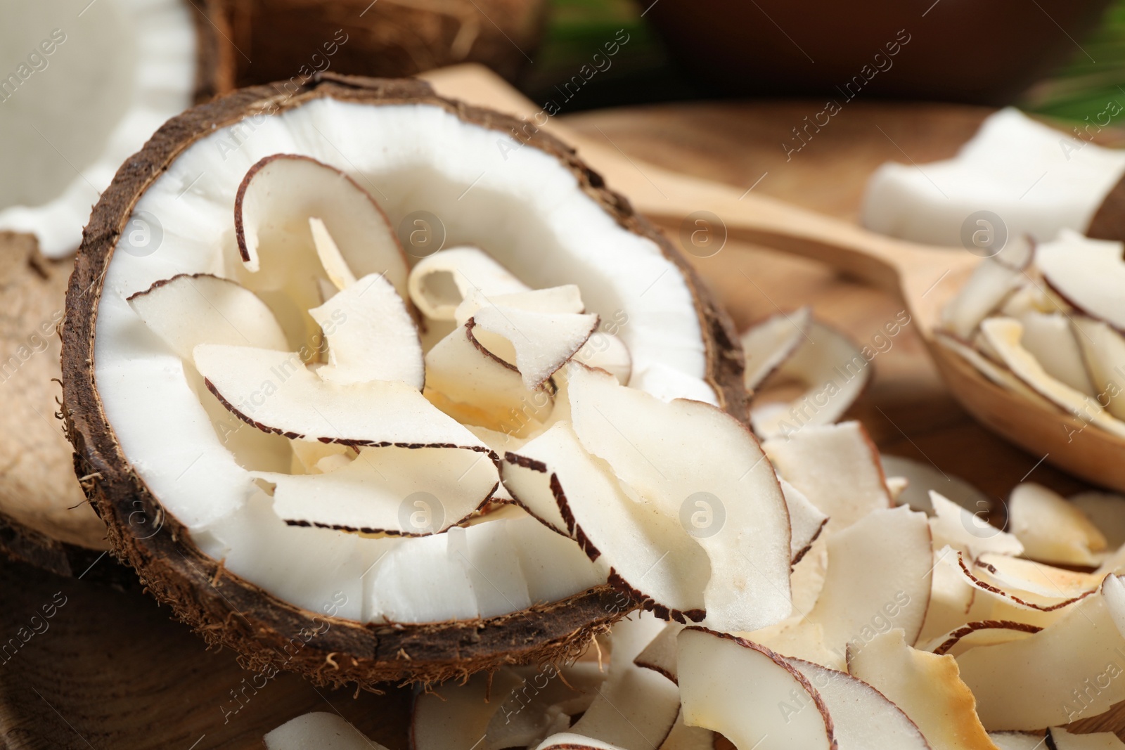 Photo of Tasty coconut chips and nut on wooden plate, closeup