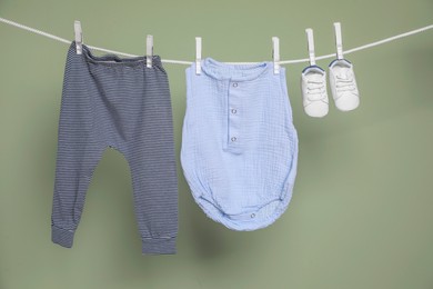 Photo of Cute small baby shoes and clothes hanging on washing line against green background