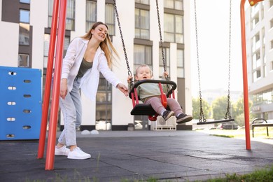 Happy nanny and cute little boy on swing outdoors