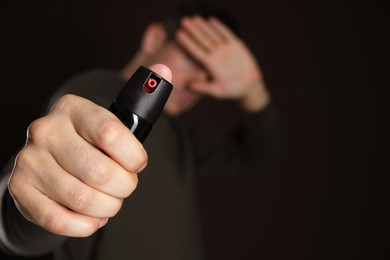Photo of Man covering eyes with hand and using pepper spray on black background, focus on canister