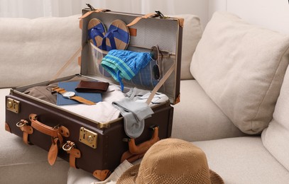 Photo of Open suitcase with different men clothes and accessories on sofa