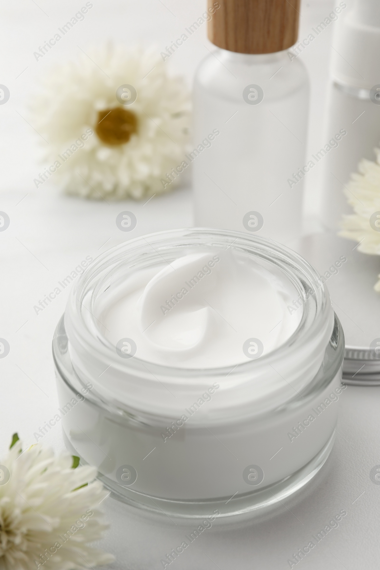 Photo of Glass jar of face cream, different cosmetic products and flowers on white marble table