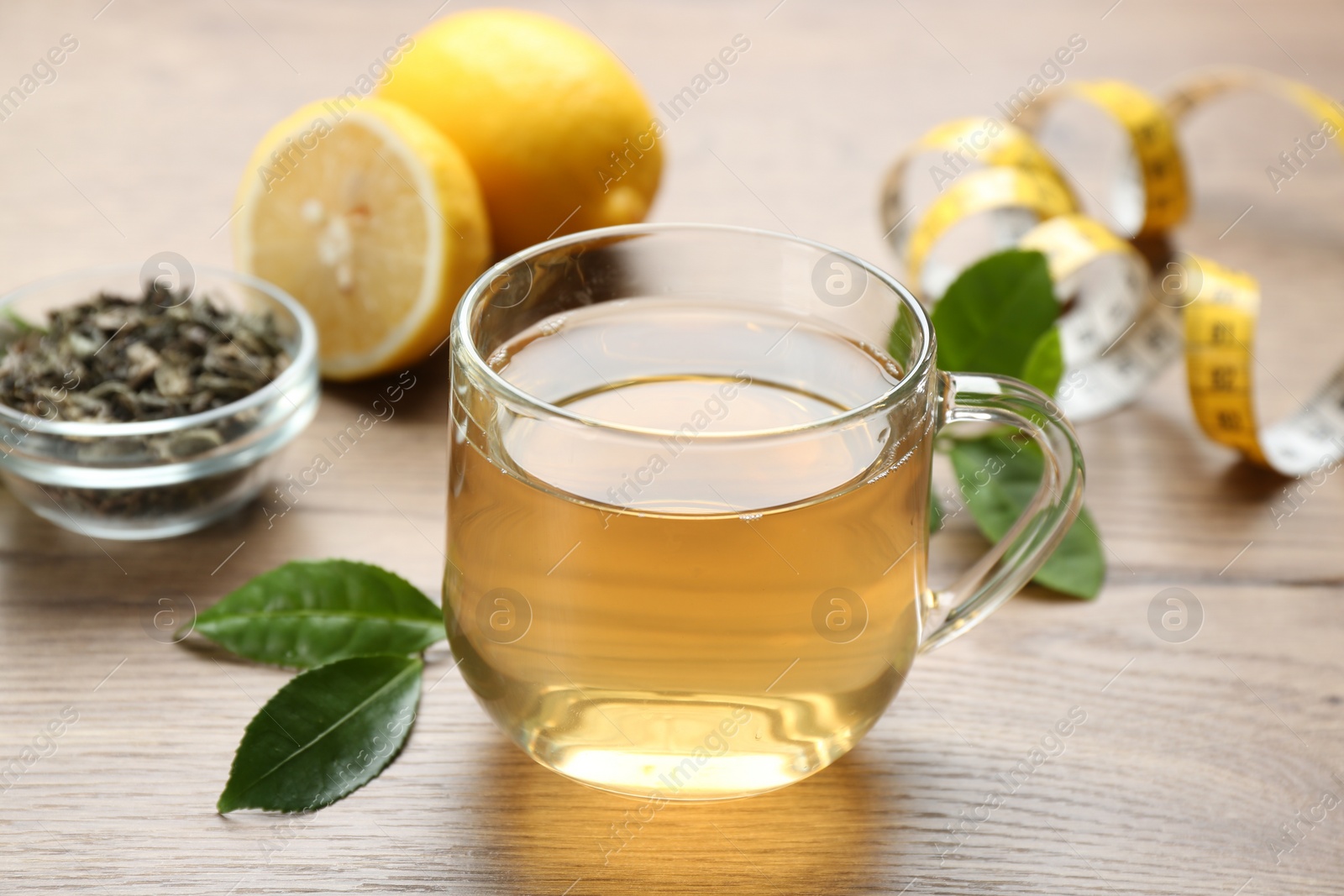 Photo of Herbal diet tea, lemon and measuring tape on wooden table