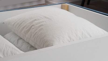 Storage drawer under bed with white pillows indoors, closeup