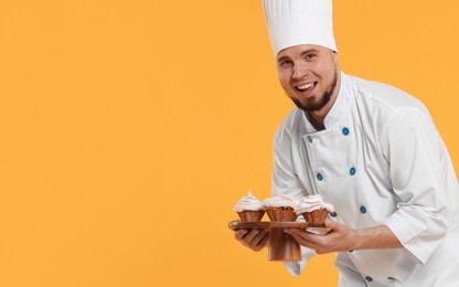 Photo of Happy professional confectioner in uniform holding delicious cupcakes on yellow background. Space for text