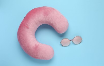 Photo of Pink travel pillow and sunglasses on light blue background, flat lay