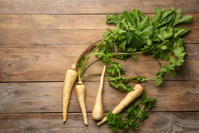 Photo of Fresh ripe parsnips with leaves on wooden table, flat lay. Space for text