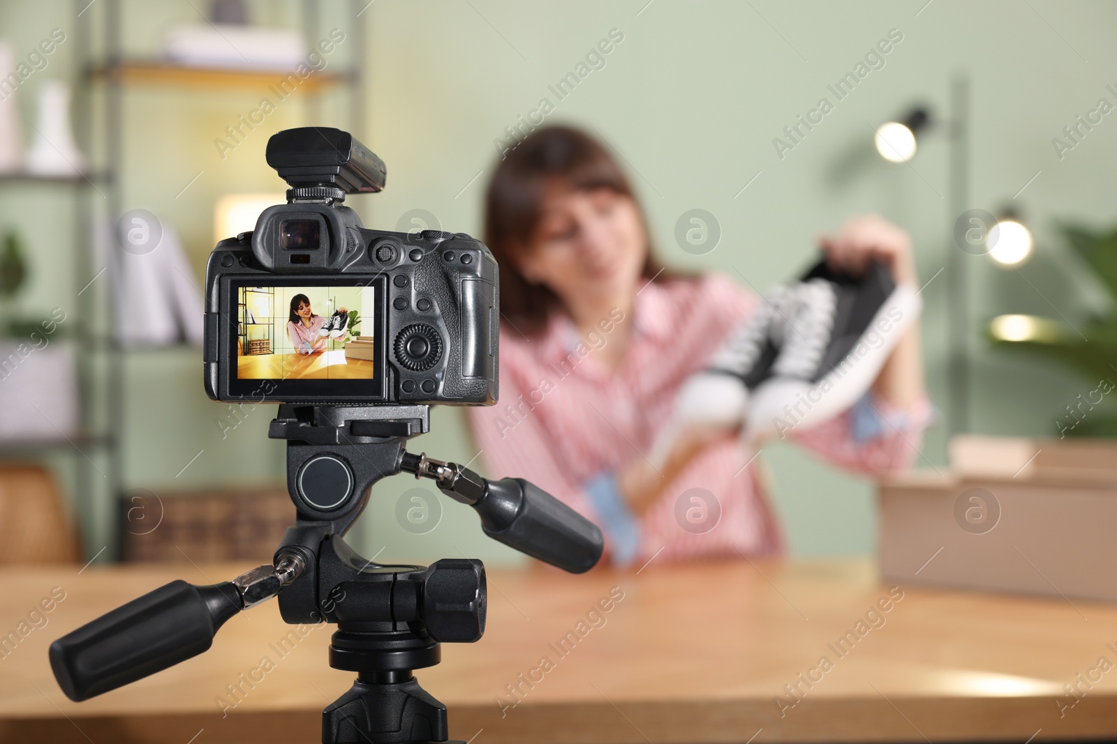 Photo of Fashion blogger recording video while talking about sneakers at home, focus on camera