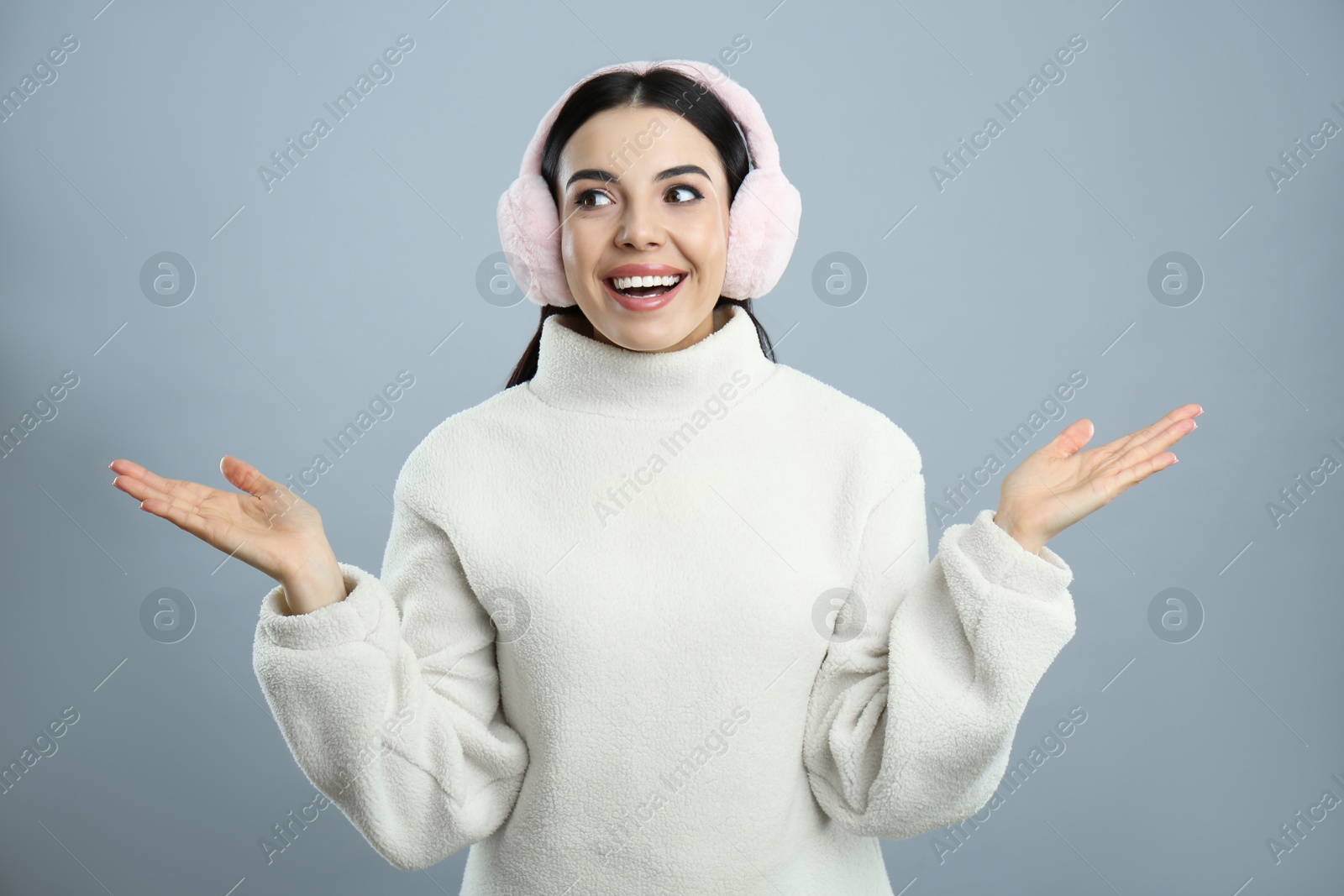 Photo of Beautiful young woman wearing earmuffs on light grey background