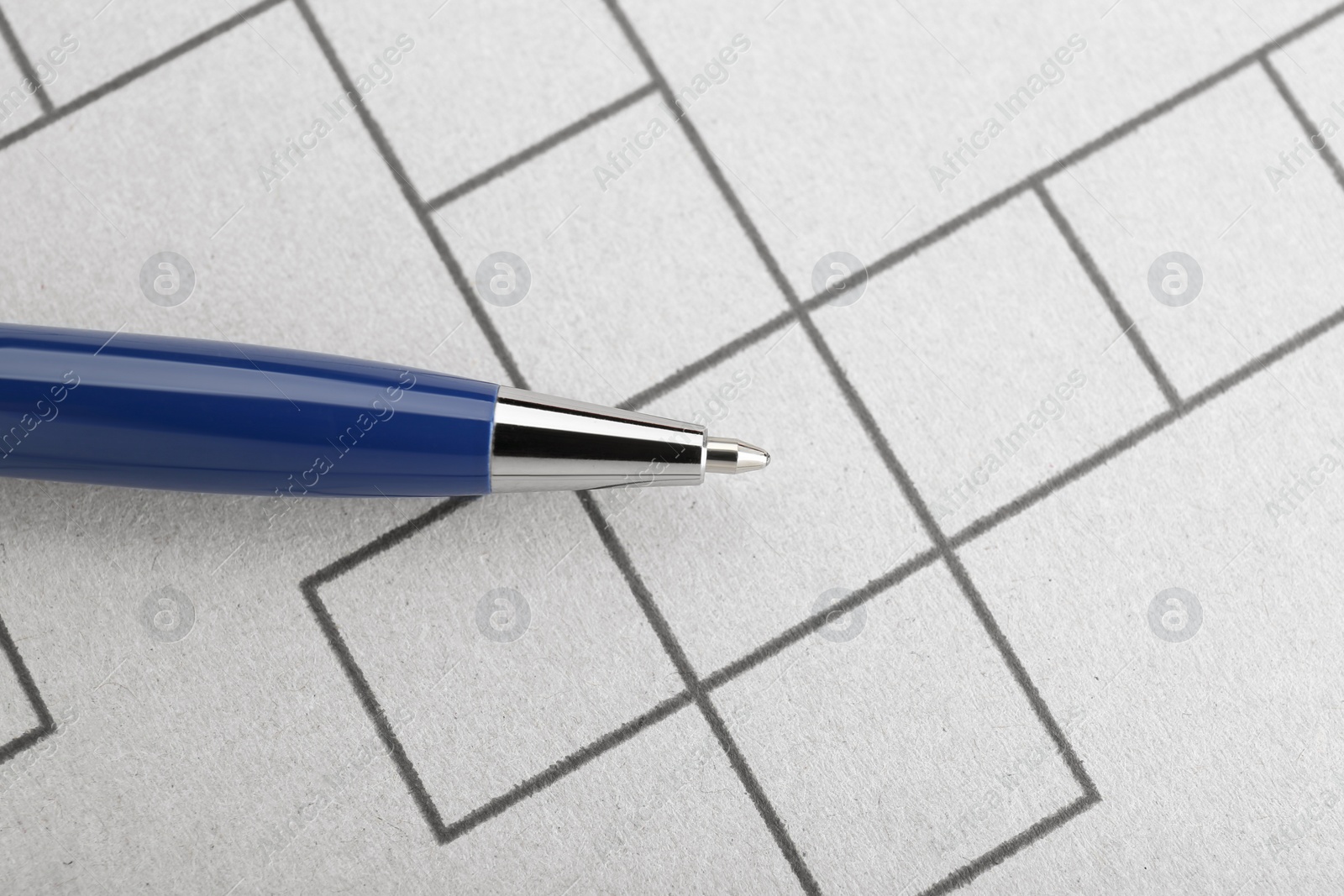 Photo of Pen on blank crossword, top view. Intellectual entertainment