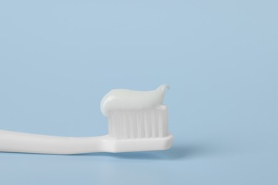 Plastic toothbrush with paste on light blue background, closeup