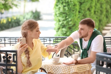 Photo of Young couple arguing while sitting in cafe, outdoors. Problems in relationship