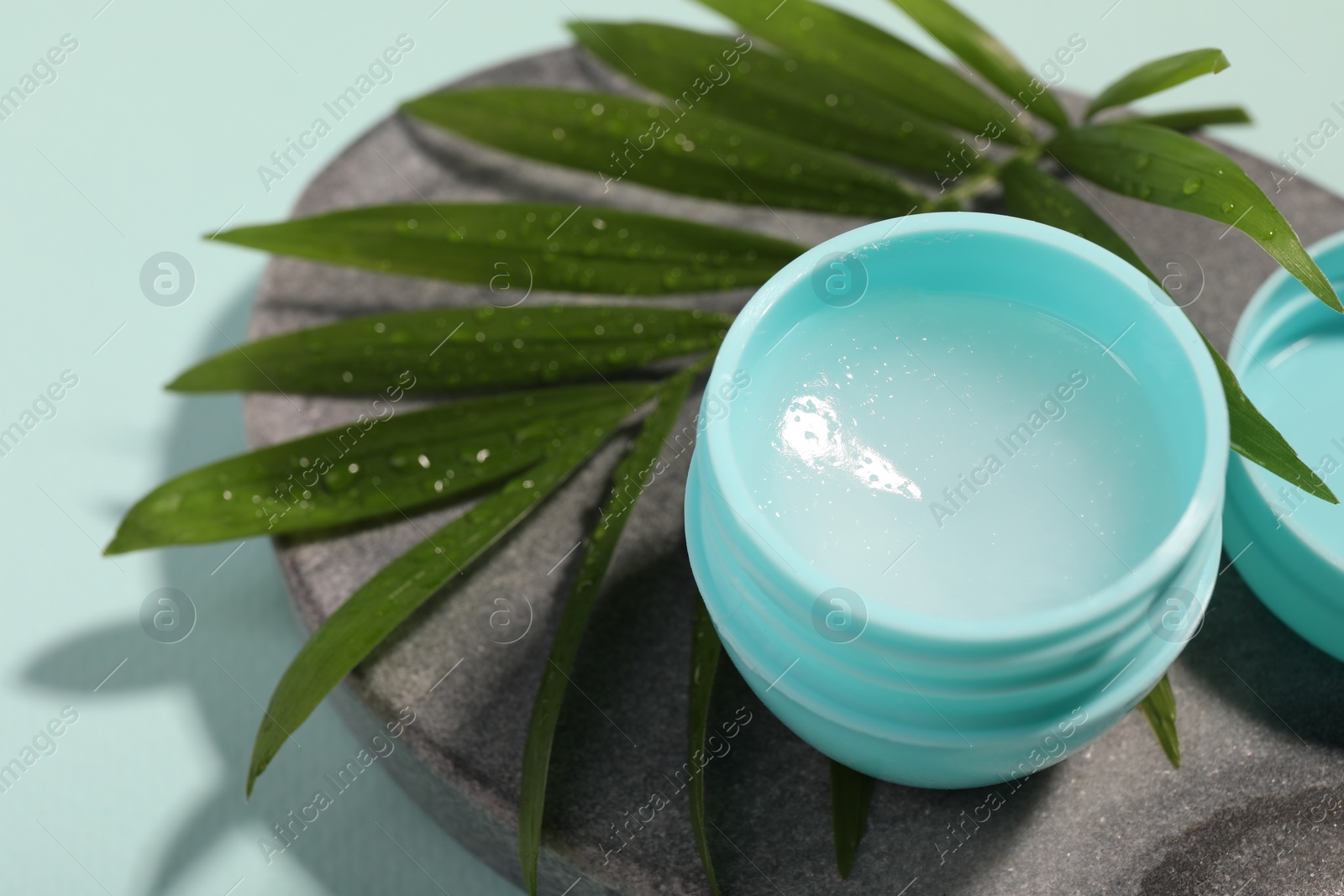 Photo of Lip balm and palm leaf on light blue background, closeup