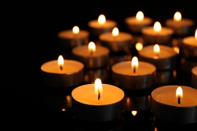 Many burning tea candles on black background, closeup