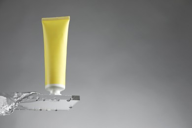 Photo of Moisturizing cream in tube on glass with water drops against grey background, low angle view. Space for text