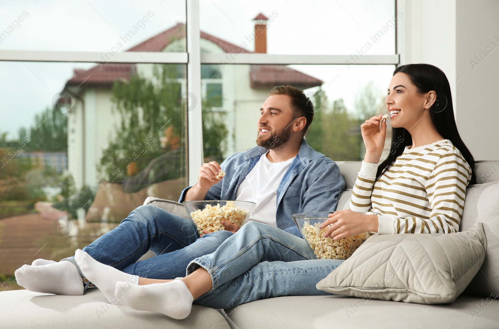 Photo of Happy couple watching movie with popcorn at home