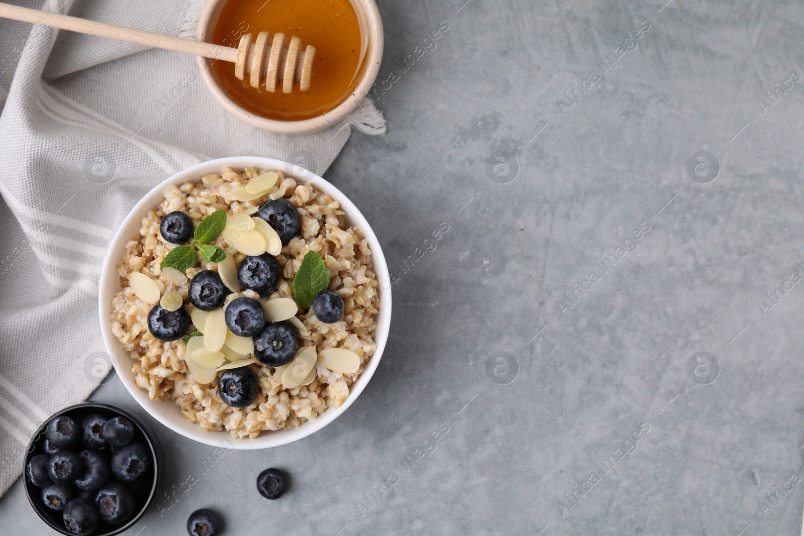 Photo of Tasty oatmeal with blueberries, mint and almond petals in bowl on grey table, flat lay. Space for text