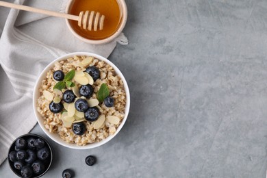 Photo of Tasty oatmeal with blueberries, mint and almond petals in bowl on grey table, flat lay. Space for text