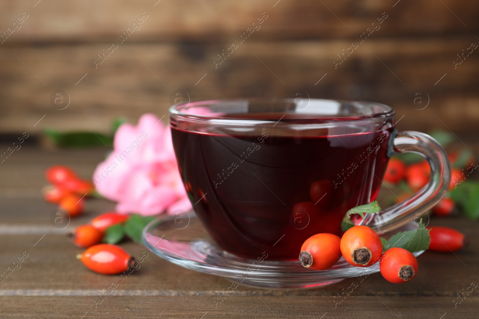 Photo of Aromatic rose hip tea and fresh berries on wooden table, closeup