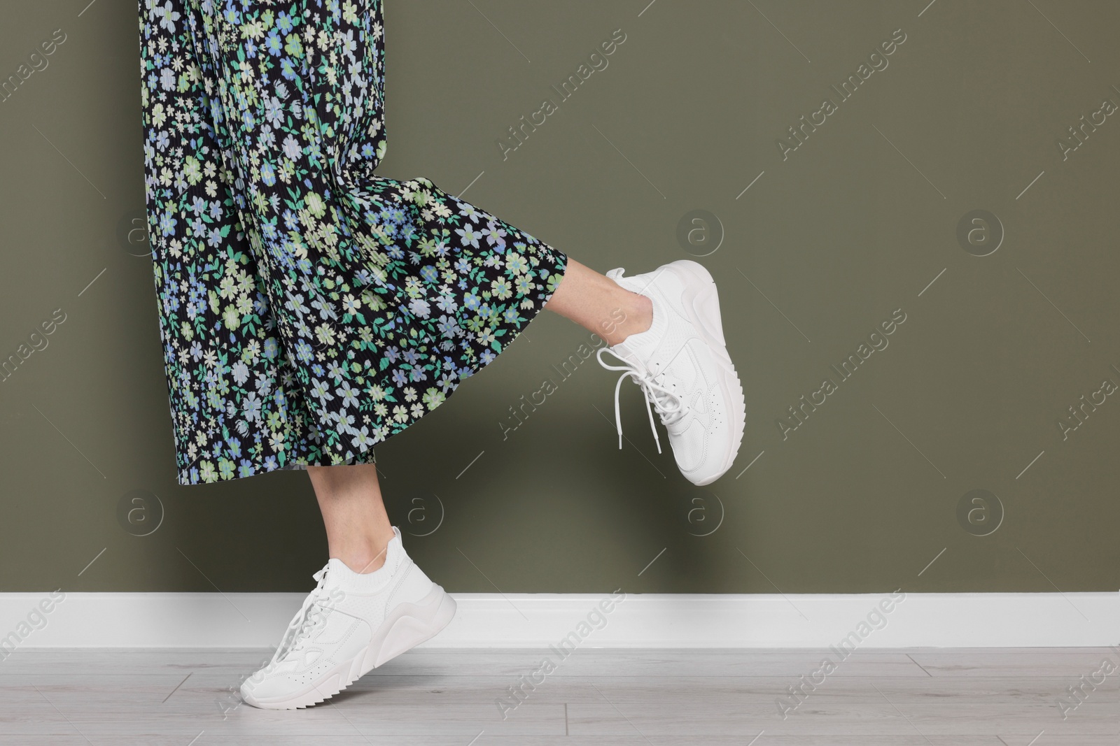 Photo of Woman wearing pair of new stylish sneakers near dark olive wall, closeup. Space for text
