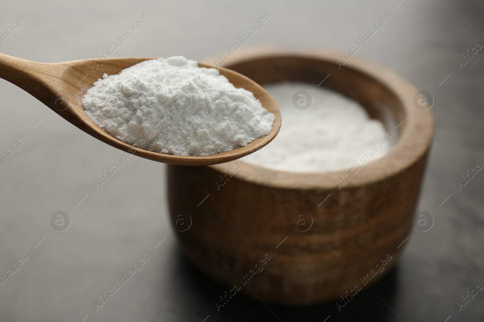 Photo of Spoon of baking powder over bowl at grey textured table, closeup. Space for text