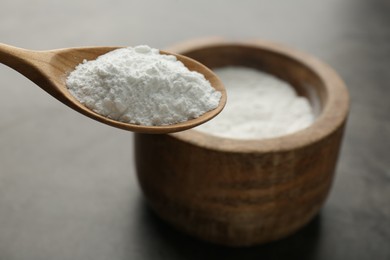 Photo of Spoon of baking powder over bowl at grey textured table, closeup. Space for text