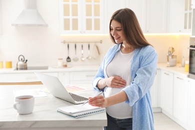 Pregnant woman working in kitchen at home. Maternity leave