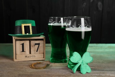 Photo of St. Patrick's day celebrating on March 17. Green beer, block calendar, leprechaun hat, horseshoe and decorative clover leaf on wooden table