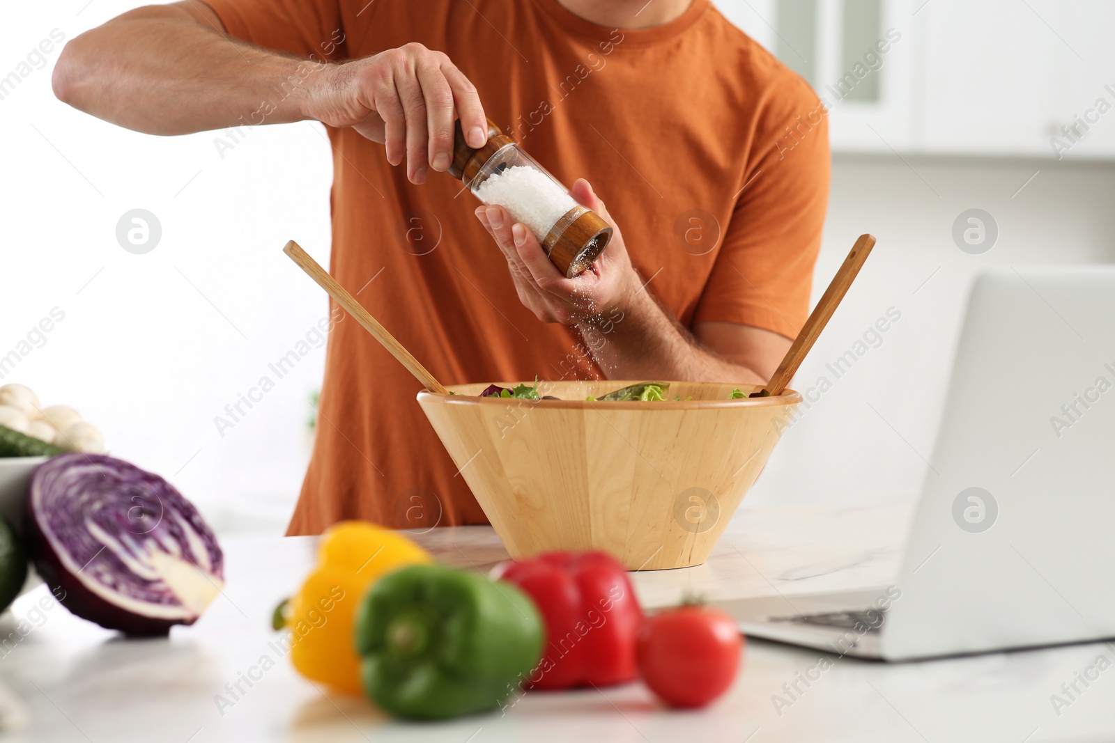 Photo of Man making dinner while watching online cooking course via laptop in kitchen, closeup