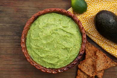 Delicious guacamole, avocados and nachos on wooden table, flat lay