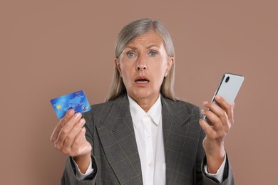 Shocked businesswoman with credit card and smartphone on brown background. Be careful - fraud