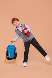 Happy schoolboy with book and backpack on beige background