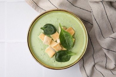 Photo of Delicious spinach cream soup with croutons in bowl on white tiled table, top view