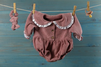 Photo of Baby clothes and accessories hanging on washing line near light blue wooden wall