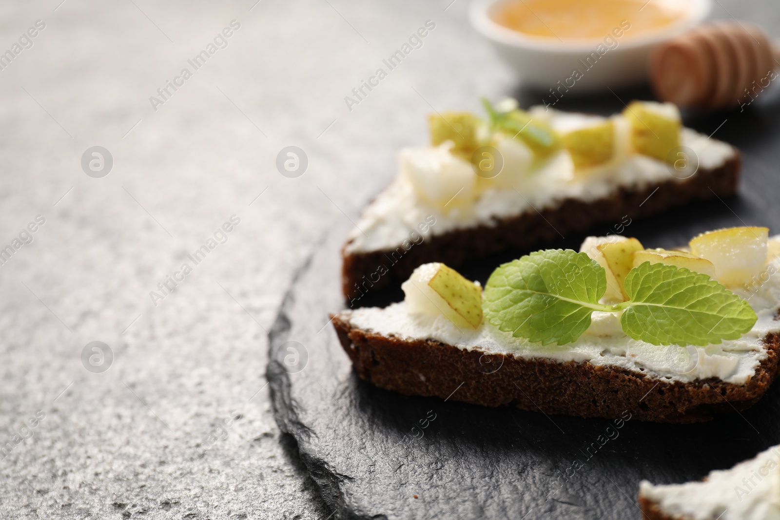 Photo of Delicious bruschetta with ricotta cheese, pear and mint on grey textured table, closeup. Space for text