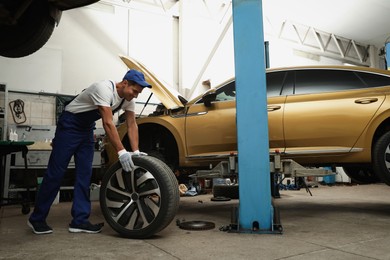 Photo of Professional mechanic with car wheel at automobile repair shop