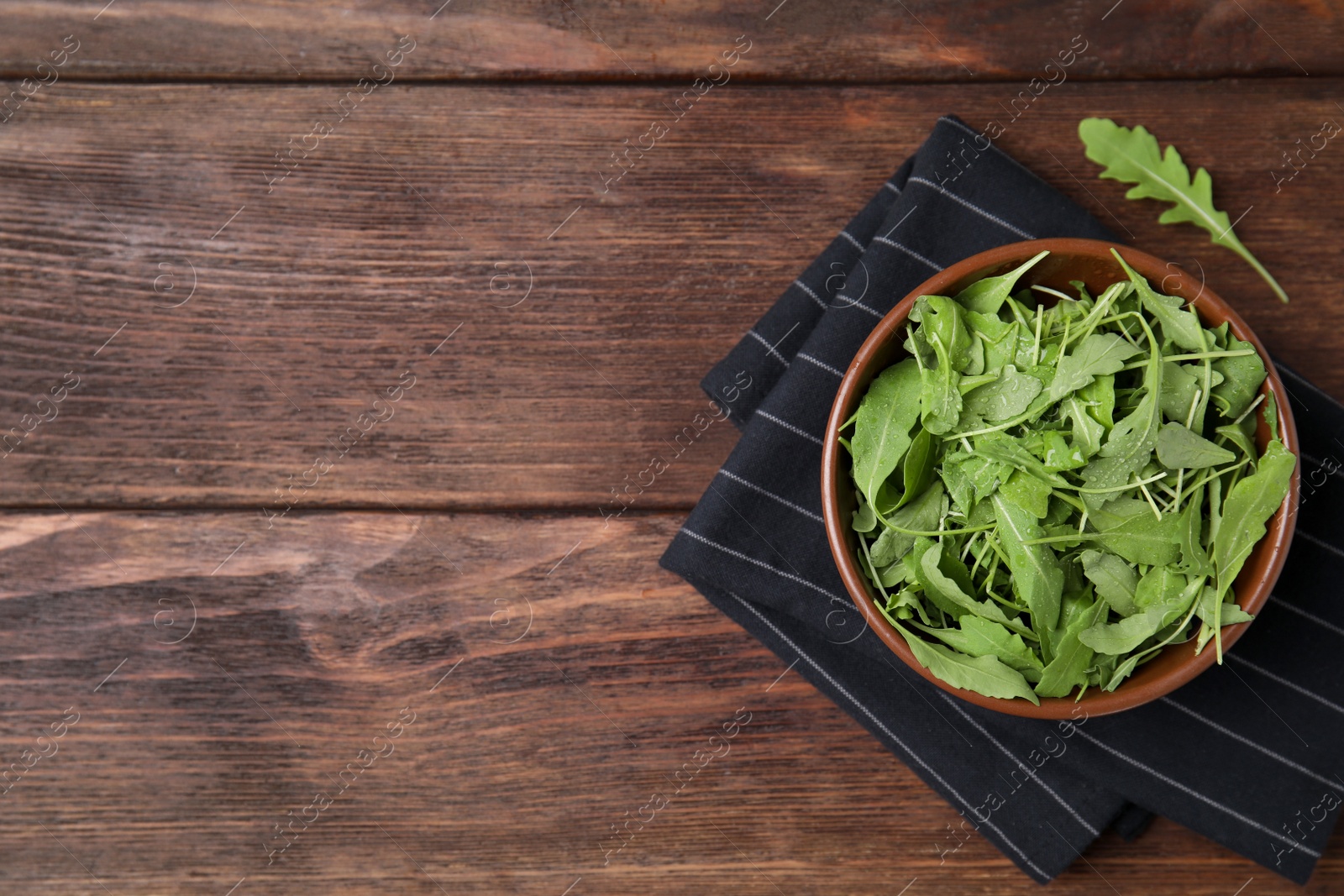 Photo of Fresh arugula leaves in bowl on wooden table, flat lay. Space for text