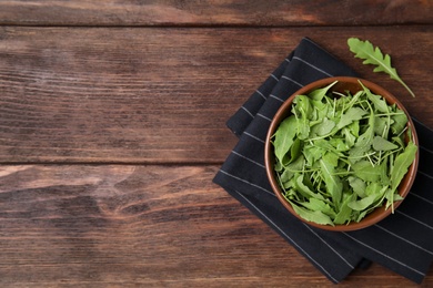 Fresh arugula leaves in bowl on wooden table, flat lay. Space for text